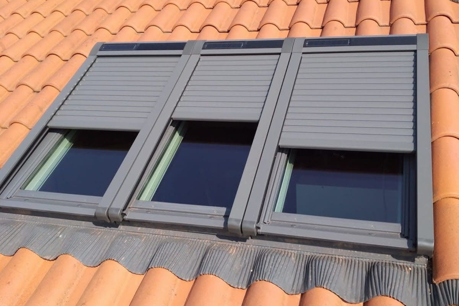 Fenêtre de toit avec volets roulants sur tuiles rouges.
