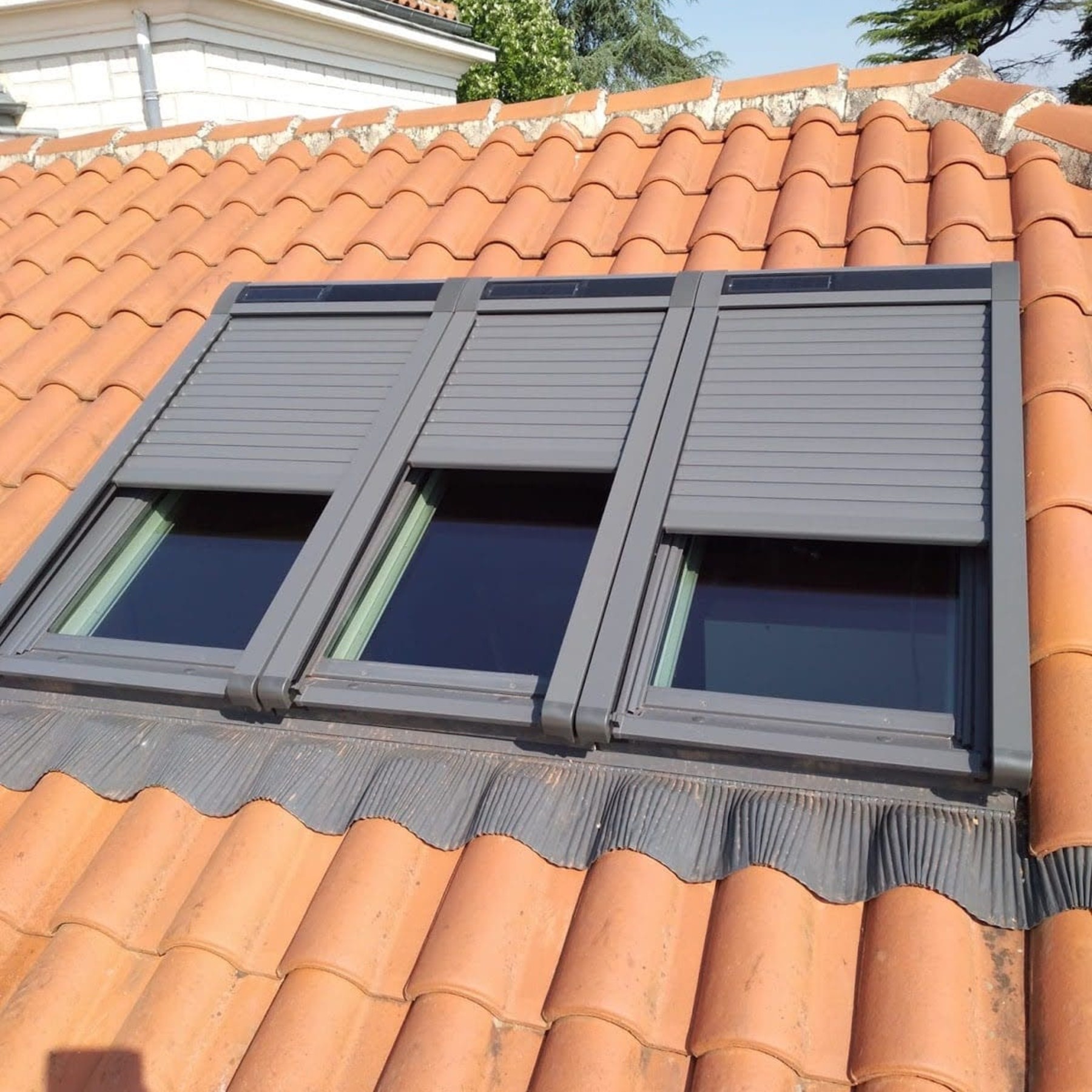 Fen&ecirc;tre de toit avec volets roulants sur tuiles rouges.